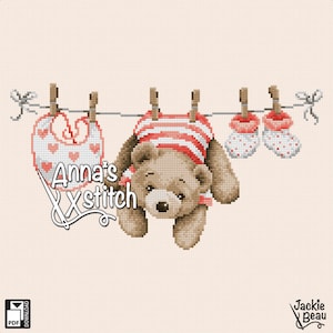 以下が含まれることがあります： 赤い白のストライプのロンパースを着た茶色のテディベア、ハート柄のピンクのスタイ、ピンクのベビーシューズのクロスステッチパターン。アイテムは洗濯ばさみで洗濯ロープにかけられています。