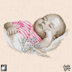 以下が含まれることがあります： ピンクと白のストライプの毛布に包まれた眠っている赤ちゃんのクロスステッチパターン。パターンは「Anna's Xstitch」というタイトルです。