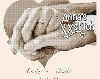May include: A cross-stitch pattern of two hands holding each other, with a ring on one finger. The hands are in a heart shape, and the text "Anna's Xstitch" is above them. The text "Emily - Charlie 12-04-2021" is below the hands.