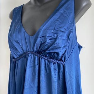 May include: A sleeveless, navy blue nightgown with a V-neckline. The bodice features a gathered design with a braided trim detail. The fabric has a slight sheen, and the garment is displayed on a mannequin.