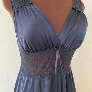 May include: A navy blue nightgown with a V-neckline and a fitted waist. The nightgown features lace detailing on the straps and waist, and a small bow at the bust. The fabric has a slight sheen.