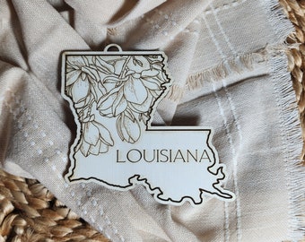 May include: Wooden ornament shaped like the state of Louisiana with a floral design and the word "LOUISIANA" inscribed on the bottom.