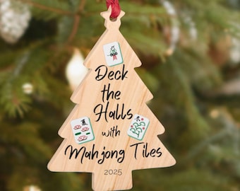Puede incluir: Adorno navideño de madera con forma de árbol, con el texto "Deck the Halls with Mahjong Tiles" y el año 2025. El adorno está suspendido por una cuerda roja y presenta ilustraciones de fichas de Mahjong.