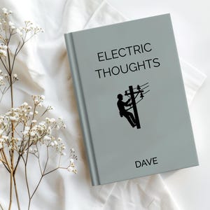 May include: A light gray book titled "ELECTRIC THOUGHTS" with a black graphic of a lineman on a utility pole. The name "DAVE" is printed at the bottom. The book is on a white surface with white flowers.