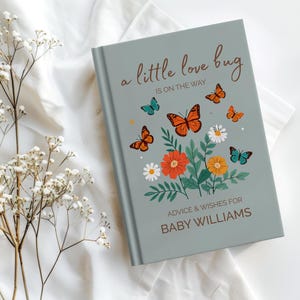 May include: A light blue book with the text "a little love bug is on the way" and "advice & wishes for BABY WILLIAMS". The cover features orange and teal butterflies and flowers.