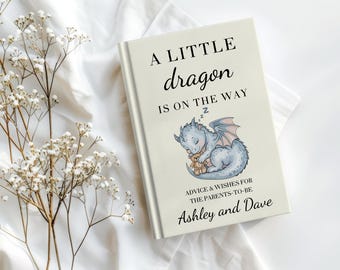 以下が含まれることがあります： クリーム色の表紙のハードカバー本。A LITTLE dragon IS ON THE WAYという文字、テディベアを抱いて眠る青いドラゴンのイラスト、ADVICE & WISHES FOR THE PARENTS-TO-BE Ashley and Daveという文字が印刷されています。