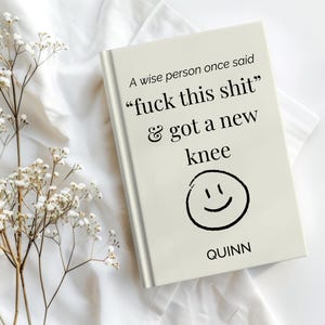 Könnte beinhalten: Ein cremefarbenes Hardcover-Buch mit dem schwarzen Aufdruck: A wise person once said "fuck this shit" & got a new knee, gefolgt von einem handgezeichneten schwarzen Smiley-Gesicht und dem Namen QUINN, der unten auf dem Einband zentriert ist.