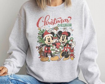 May include: A gray sweatshirt with a vintage-style Christmas design featuring Mickey and Minnie Mouse. The text on the sweatshirt reads "Christmas on Main Street".