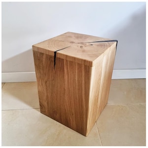 Puede incluir: Un taburete cuadrado de madera con un acabado de madera natural y una grieta negra que atraviesa la parte superior.