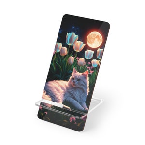 May include: A white cat with blue eyes sits in a field of glowing pink and blue tulips under a full moon. The cat is looking to the right of the image. The background is a dark blue night sky with stars.