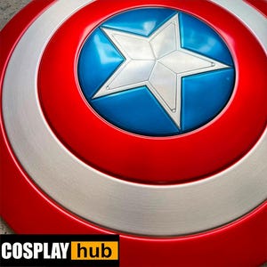 Pu&ograve; includere: Primo piano di uno scudo di Captain America. Lo scudo presenta una combinazione di colori rosso, bianco e blu con una grande stella bianca al centro. Lo scudo ha un design circolare con anelli concentrici di colore. Il testo "COSPLAY hub" &egrave; in basso a sinistra.