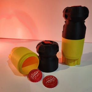 May include: A selection of 3D-printed objects, including a yellow and black cylindrical container, two black and red bottle-shaped items, and two red bottle caps with "Nuka Cola" text. The items are displayed on a white surface.