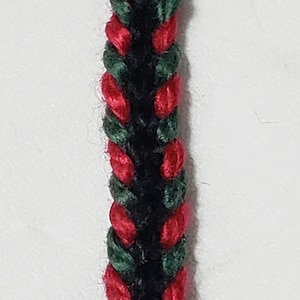 May include: A close-up of a braided cord with red, green, and black threads.