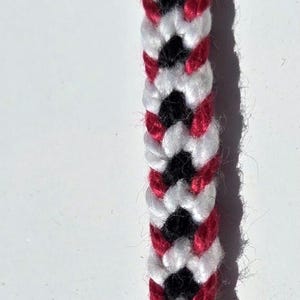 May include: A close-up of a red, white, and black friendship bracelet with a braided pattern.