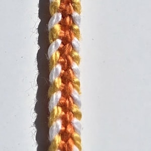 May include: A close-up of a braided cord with orange, yellow, and white stripes.