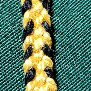 May include: A close-up of a braided rope with alternating black and yellow strands. The rope is against a green background.