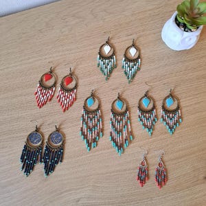 Può includere: Una collezione di orecchini di perline in vari stili e colori. Gli orecchini presentano forme circolari e a goccia, con frange di perline rosse, bianche, turchesi e blu navy. Alcuni orecchini hanno un accento geometrico centrale.