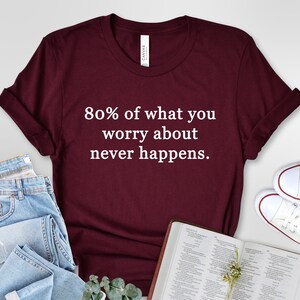 May include: Burgundy t-shirt with white text that reads "80% of what you worry about never happens."