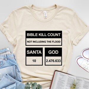 May include: A beige t-shirt with black text that reads "Bible Kill Count Not Including The Flood" and a chart with the categories "Santa" and "God" with the numbers "10" and "2,476,633" respectively.