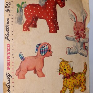 May include: A vintage Simplicity printed pattern envelope featuring illustrations of four stuffed animals: a red horse with white polka dots, a blue striped rabbit, a pink dog with plaid ears, and a yellow cat with a small red floral print pattern.