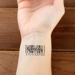 Puede incluir: Un tatuaje temporal negro con el nombre "Henry" en cursiva, integrado en un diseño de código de barras. Debajo del nombre, los números romanos "XVI•I•XXVIII". El tatuaje está en la muñeca.