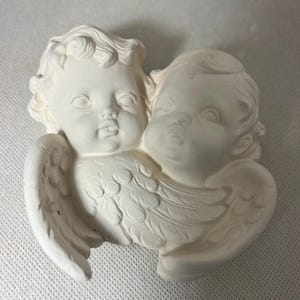 May include: White ceramic figurine of two cherubs with wings, one with its arm around the other. The cherubs have detailed facial features and are in a hugging pose.
