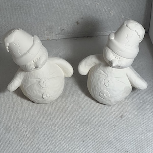May include: Two white ceramic snowman figurines with black button eyes and a red Santa hat. The snowmen are in a standing position with their arms outstretched.