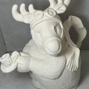 Puede incluir: Figura de reno de cerámica blanca con gafas y una bufanda, sosteniendo una taza en una mano. El reno tiene un diseño de piel texturizado y está listo para ser pintado.