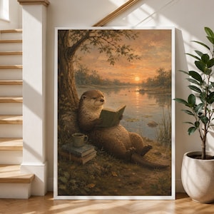 Könnte beinhalten: Ein gerahmter Wandkunstdruck, der einen braunen Otter zeigt, der bei Sonnenuntergang unter einem Baum am Fluss sitzt und ein grünes Buch liest. Ein Stapel aus zwei Büchern und eine kleine Tasse stehen auf dem Boden neben dem Otter.