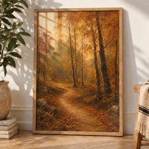 Könnte beinhalten: Ein gerahmter, rechteckiger Kunstdruck mit einem Ölgemälde eines Waldwegs im Herbst. Die Szene zeigt hohe Bäume mit goldenem und orangefarbenem Laub, einen mit Blättern bedeckten Erdweg und sanftes Sonnenlicht, das durch die Bäume fällt.