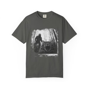 May include: A dark gray t-shirt with a black and white image of a cat looking scared with a figure of a large hairy creature behind it in the woods.