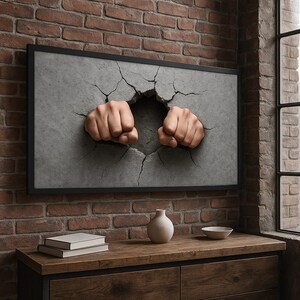 May include: A framed artwork depicts two clenched fists breaking through a gray concrete wall. The artwork is set against a red brick wall, with a wooden cabinet and decorative items in the foreground.