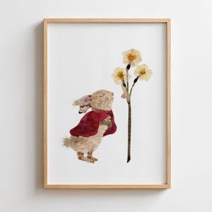 Puede incluir: Una lámina artística enmarcada que presenta un collage hecho con pétalos de flores secas prensadas. La imagen muestra a un conejo con una capa de color rojo oscuro, de pie frente a un tallo fino con tres flores de color amarillo pálido.