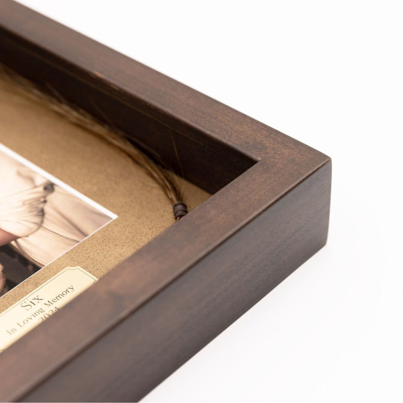 May include: A brown wooden frame with a matted opening. A strand of hair is displayed in the frame with a small tag that reads "Six In Loving Memory 2024".
