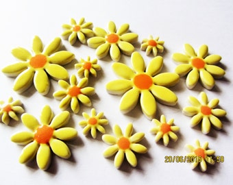 Puede incluir: Un conjunto de adornos amarillos con forma de margarita y centros naranjas. Las flores, de diferentes tamaños, están dispuestas sobre una superficie blanca. Los pétalos son lisos y redondeados, creando un efecto alegre y brillante.