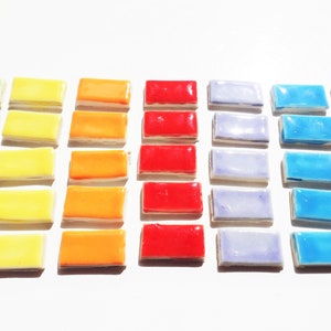 May include: A set of 40 small rectangular ceramic tiles in a rainbow color gradient. The tiles are arranged in rows, starting with green, then yellow, orange, red, purple, blue, and pink.