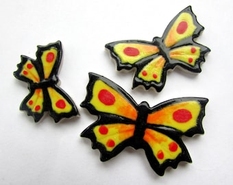 Puede incluir: Tres azulejos de cerámica con forma de mariposa con contornos negros y alas amarillas y naranjas con puntos rojos.
