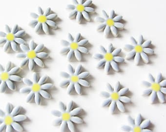 Puede incluir: Una colección de 17 azulejos de cerámica con forma de margarita en tonos azules y amarillos. Los azulejos tienen un diámetro aproximado de 2,5 cm y una superficie ligeramente texturizada.