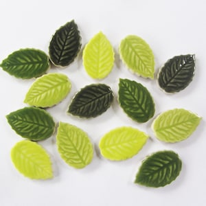 May include: A collection of ceramic leaf tiles in shades of green and yellow. The leaves are arranged in a random pattern on a white background.