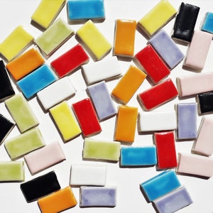 Puede incluir: Surtido de azulejos de cerámica coloridos en varias formas y tamaños. Los azulejos están dispuestos en un patrón aleatorio sobre una superficie blanca. Los azulejos son perfectos para proyectos de manualidades, decoración del hogar y arte de mosaico.