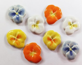 May include: Nine ceramic flower embellishments in various colors, including blue, white, yellow, and orange. Each flower has a five-petal design with a center detail.