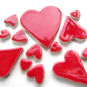 May include: A collection of red heart-shaped ceramic tiles. The tiles are various sizes and shapes, with some being more rounded and others more pointed.