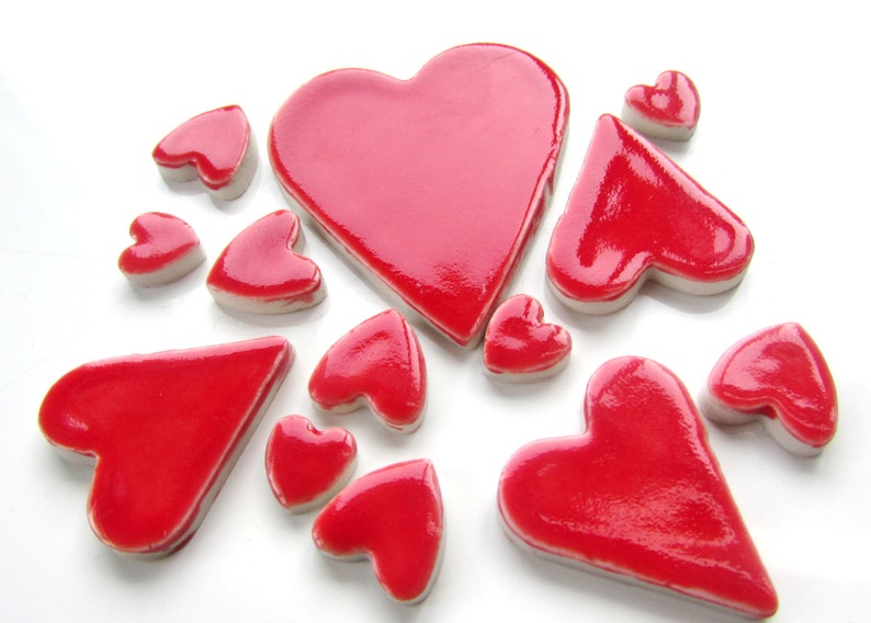 May include: A collection of red heart-shaped ceramic tiles. The tiles are various sizes and shapes, with some being more rounded and others more pointed.