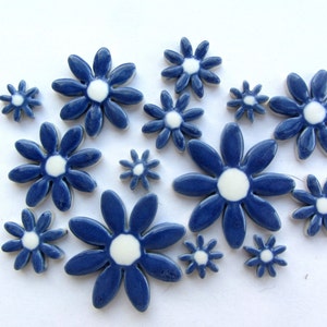 Könnte beinhalten: Eine Sammlung blauer Keramikblumenfliesen mit weißen Zentren. Die Fliesen sind unterschiedlich groß und bilden eine dynamische Anordnung. Die Blumen haben eine glänzende Oberfläche und sind auf einer weißen Oberfläche angeordnet.