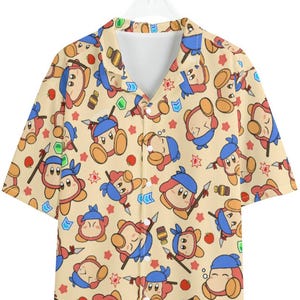 May include: Short-sleeved button-down shirt with a repeating pattern of cartoon characters in various poses. The shirt features a beige background with red, blue, and brown character illustrations. The collar and buttons are white.