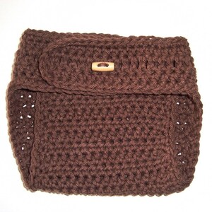 Puede incluir: Una cubierta de pañal de ganchillo marrón con un botón de madera.