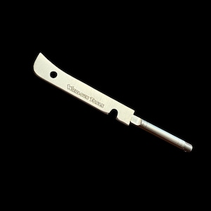 May include: A silver metal tool with a curved blade, a hole, and the text "WARLOCK TOOLS." The tool has a cylindrical handle with a threaded end. The tool is designed for a specific purpose.