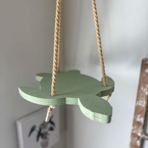 May include: A light green wooden turtle-shaped hanging planter with natural rope.