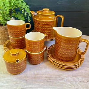 May include: A brown and orange patterned tea set with a teapot, milk jug, sugar bowl, cups, and saucers.