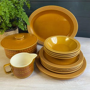 May include: A set of brown and orange vintage ceramic dinnerware, including a serving dish, a covered casserole dish, a jug, and a stack of bowls and plates.
